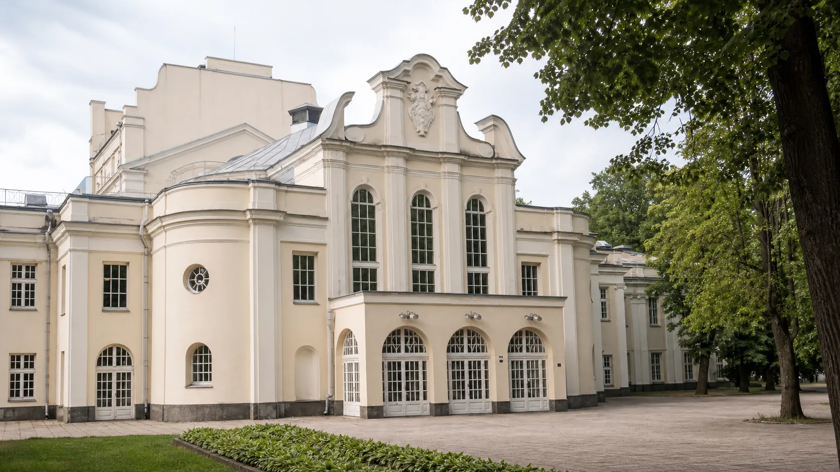 Kauno valstybinio muzikinio teatro kremiškas neobarokinis fasadas Miesto sode su trimis arkiniais langais, banguotu frontonu ir medžiais