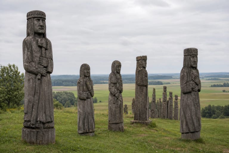 Weathered oak folk sculptures of Ablinga Memorial on a grassy rural hillside near Žvaginiai