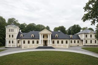Restored pale Abromiškės Manor palace with a timber central range, columned portico, tower, and masonry wings in a mature park