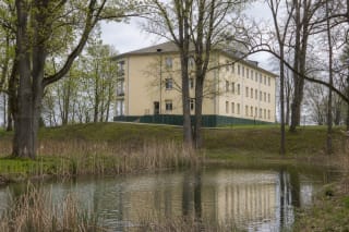 Светлый каменный дворец усадьбы Адакавас за прудом и старыми деревьями парка