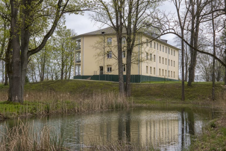 Adakavo dvaro šviesūs mūriniai rūmai už tvenkinio ir seno parko medžių