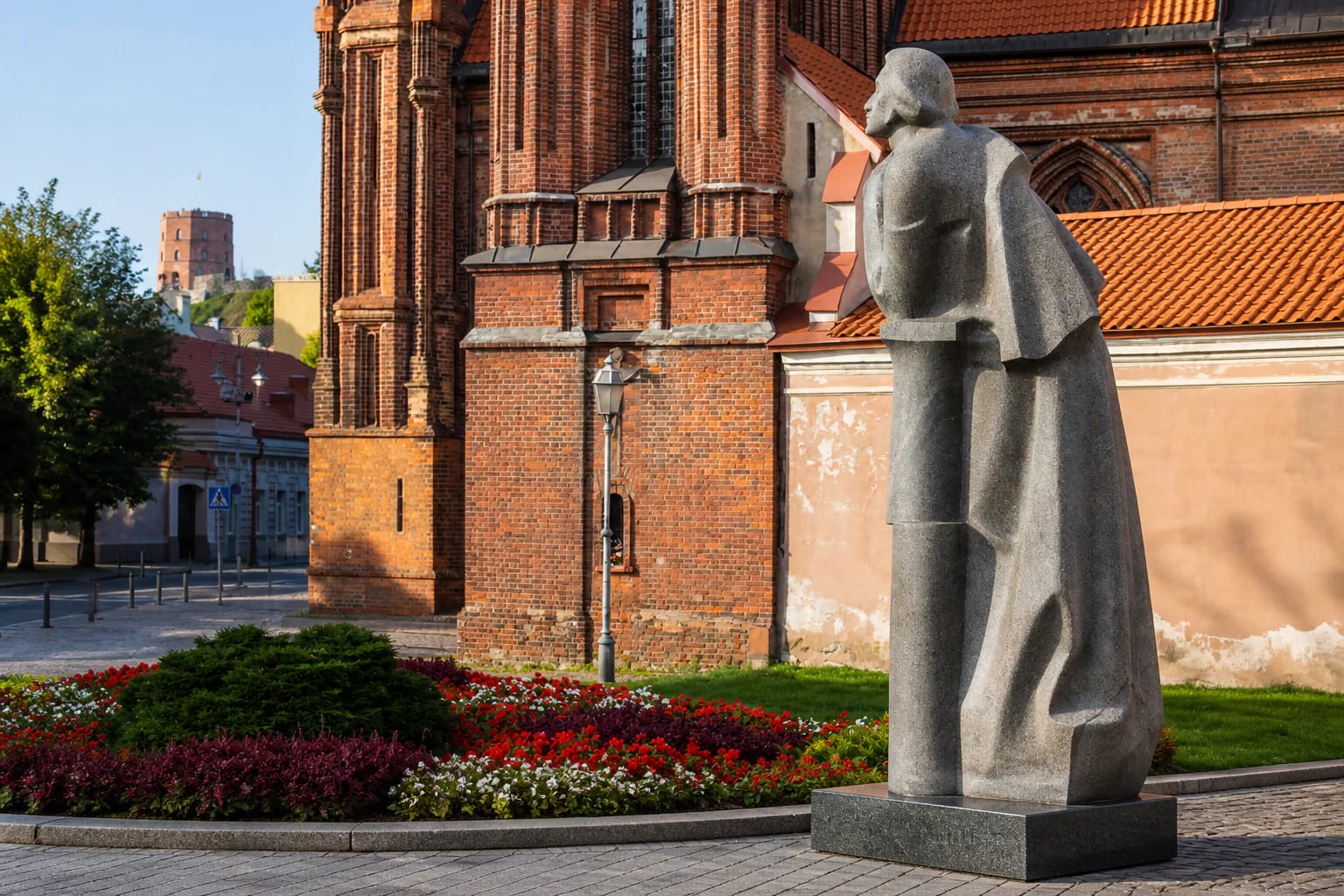 Grey-granite Adam Mickiewicz Monument beside a red-brick Gothic church in Vilnius