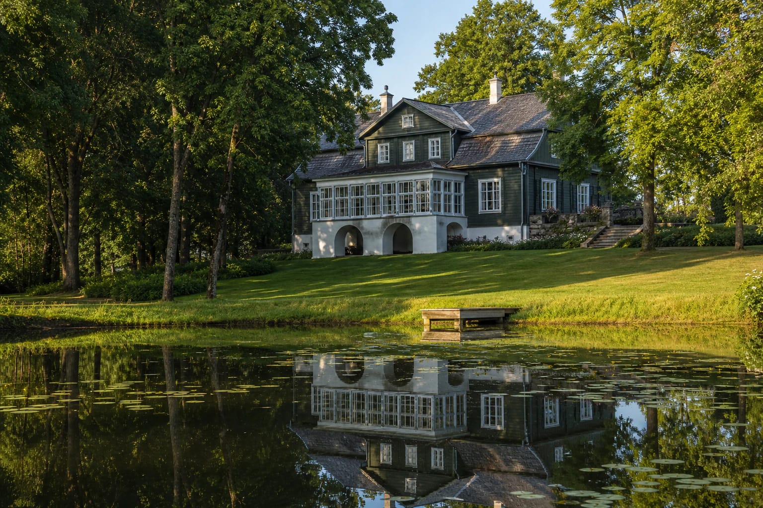 Wooden Adomynė Manor with white arched foundations reflected in a park pond