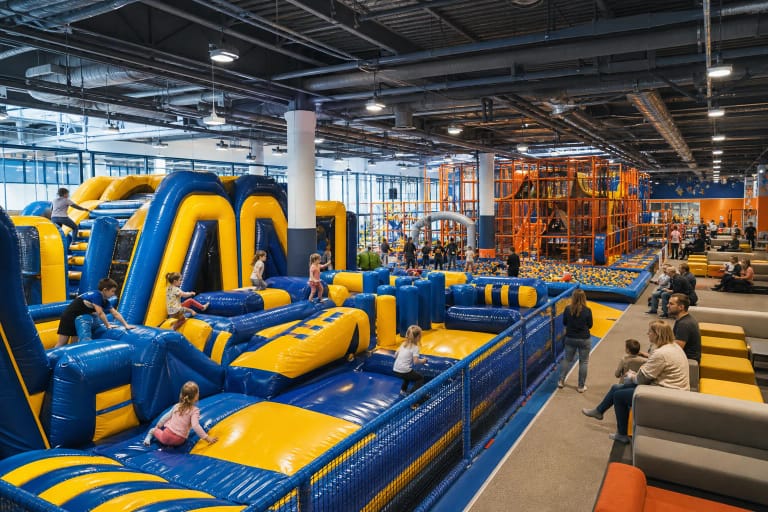 Adventica Vilnius hall with a blue-and-yellow inflatable obstacle area, orange climbing structure, and children playing