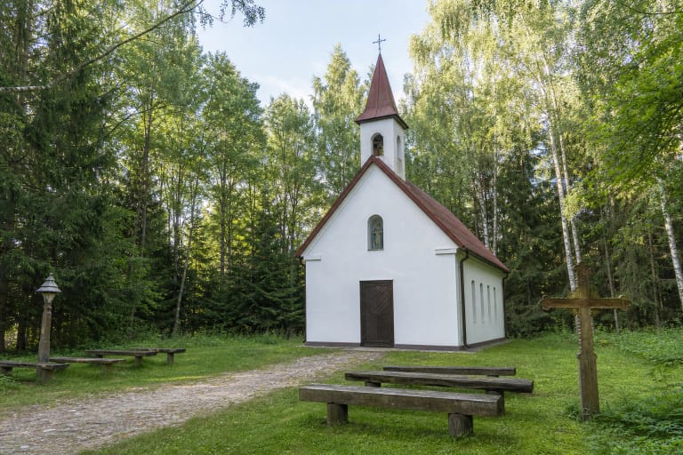 White Agailiai Forest Chapel with a red roof and belfry in a woodland clearing
