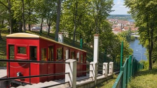 Red Aleksotas Funicular car on a hillside with the Kaunas panorama behind it