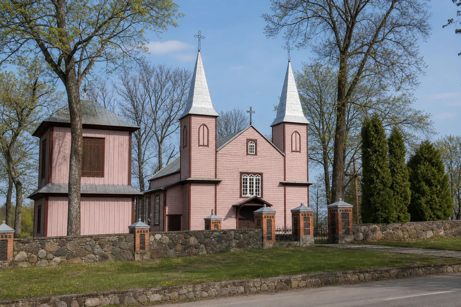 The pink Alizava wooden church with twin pointed towers and a stone wall