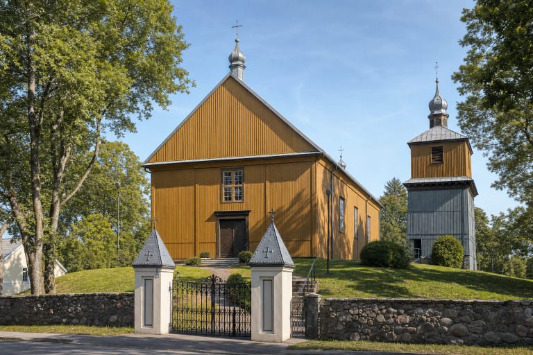 Alsėdžių medinės bažnyčios rusvai gelsvomis vertikaliomis lentomis apkaltas fasadas ant Alkos kalno, vartai ir atskira varpinė