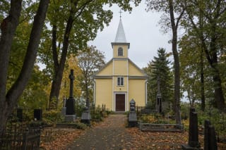 Pale yellow wooden Church of the Guardian Angels in Alytus with a tall turret and cemetery monuments in its grounds