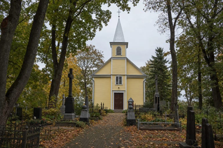 Šviesiai geltona medinė Alytaus Šv. Angelų Sargų bažnyčia su aukštu bokšteliu ir kapinių paminklais šventoriuje