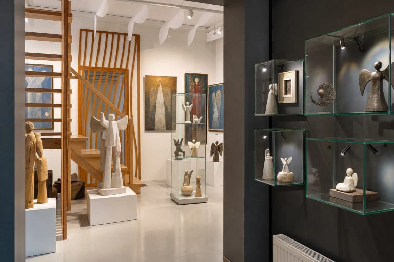 Bright Angel Museum gallery with angel sculptures in different materials displayed in glass cases and angel-themed paintings on the walls