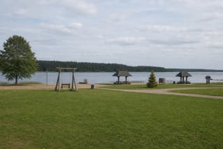 Viešasis Arino ežero paplūdimys su plačia veja, medinėmis sūpynėmis, dviem pavėsinėmis ir smėlio pakrante