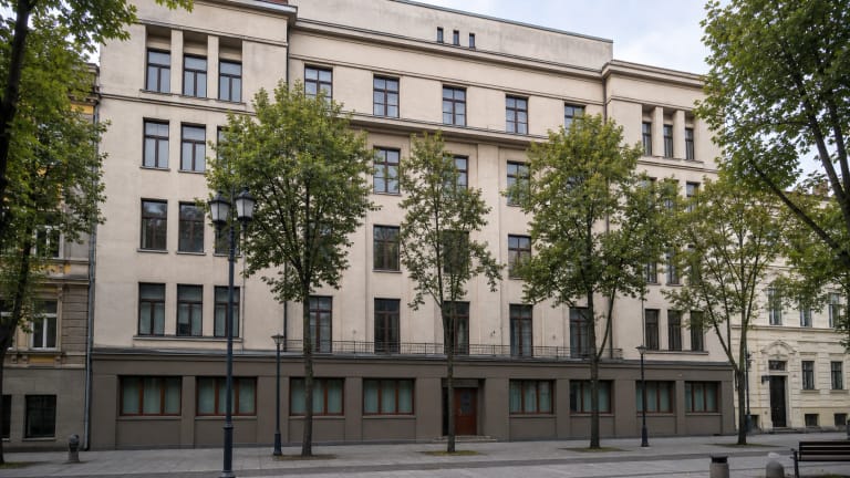 Light five-storey facade of the Ateitininkai Union Palace in Kaunas on Laisvės aleja with rectangular windows, shallow projections, and trees