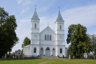 Balta Aukštadvario Kristaus Atsimainymo medinė bažnyčia su dviem bokštais, veja ir medžiais