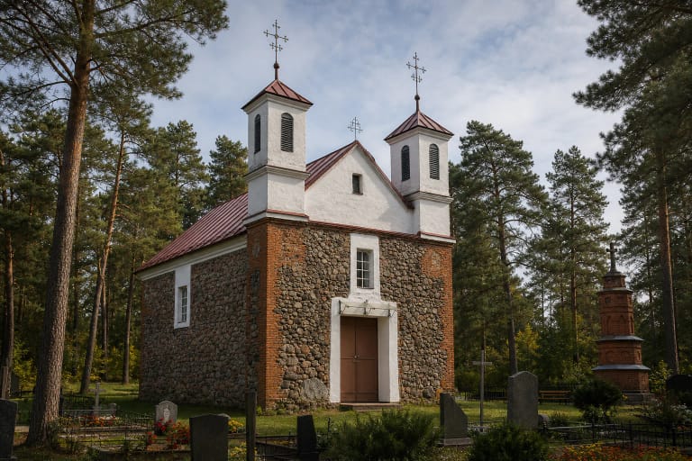 Lauko akmenų mūro Babriškių bažnyčia su raudonų plytų kampais, dviem baltais bokštais ir raudonais skardiniais stogais pušyne