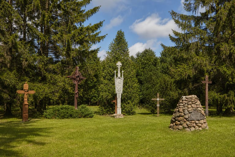 Baltijos kelio kryžių slėnio veja su lauko riedulių Laisvės aukuru ir tarp eglių išdėstytais skirtingais kryžiais