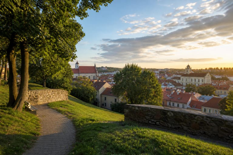 Bastėjos kalno žolėtas šlaitas ir Vilniaus senamiesčio panorama saulėlydžio šviesoje
