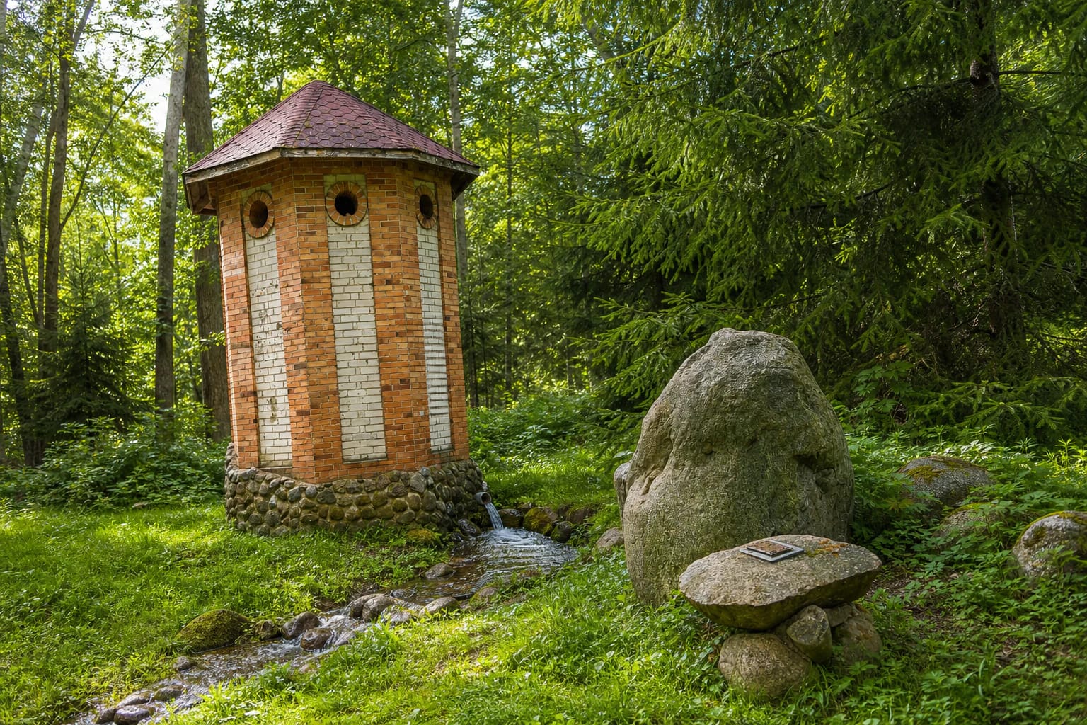 Bečiai Spring's red-and-pale-brick well-house, flowing water, and fieldstones in the former manor park