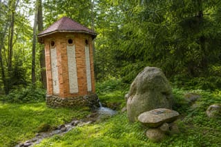 Bečiai Spring's red-and-pale-brick well-house, flowing water, and fieldstones in the former manor park