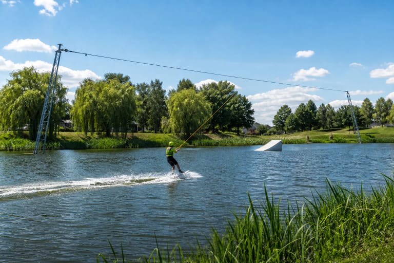 Vandenlentininkas Birštonas Wake Park trasoje tarp dviejų kabelio atramų ir žalio ežerėlio kranto