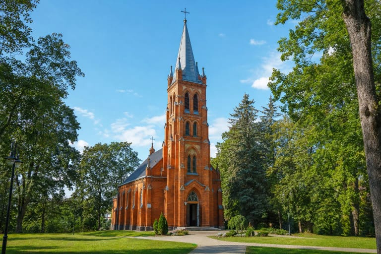 Red-brick Church of St Anthony of Padua in Birštonas with its single tall Gothic Revival tower in a green churchyard