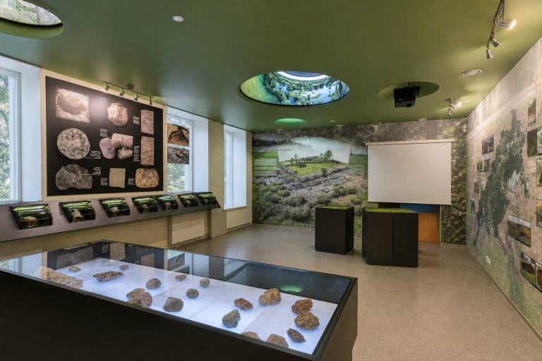 Green geology gallery inside Biržai Regional Park Visitor Centre, with a rock display case and sinkhole-like ceiling forms