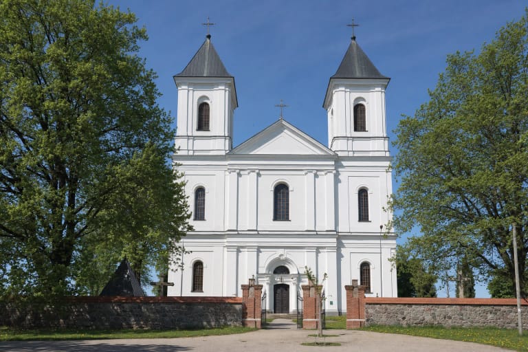 Balta dvibokštė Biržų Šv. Jono Krikštytojo bažnyčia už žalios Nepriklausomybės aikštės