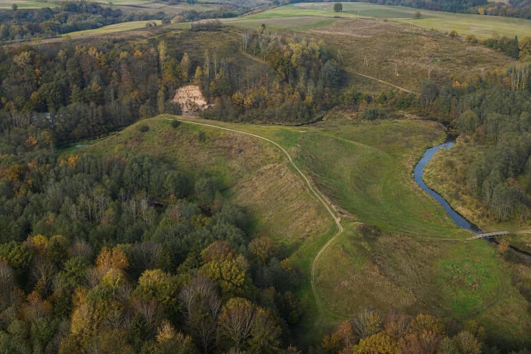 Aerial view of the green Bradeliškės Hillfort promontory enclosed on three sides by the winding Dūkšta and a wooded valley