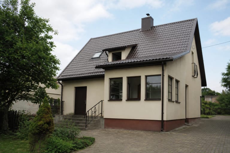 Asimetriškas Brazauskų namų ekspozicijos šoninis fasadas su tamsiu stogu, langais ir lauko laiptais
