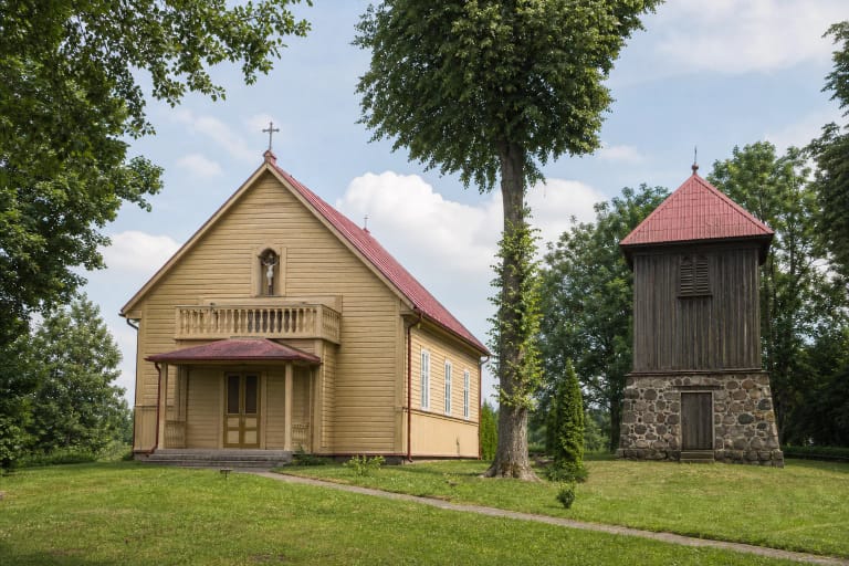 Geltona medinė Butrimonių Šv. arkangelo Mykolo bažnyčia su raudonu stogu, medžiais ir atskira varpine