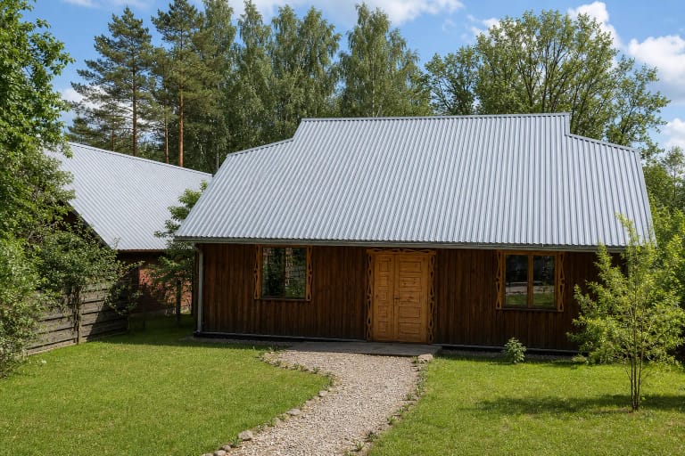 Čekauskų etnografijos muziejaus tamsaus medžio pastatas Lekėčiuose su aukštu sidabriniu metaliniu stogu, drožinėtomis durimis ir sodo taku