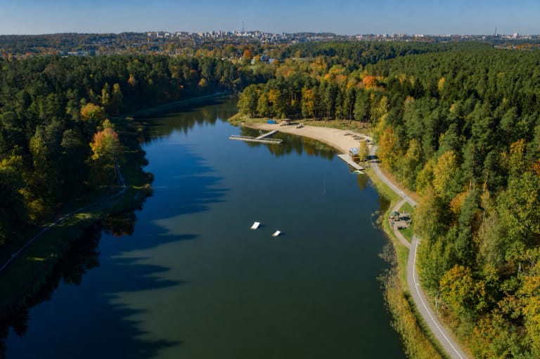 Didžioji Dailidė Alytaus Kurorto parko pušyne iš oro, su smėlio paplūdimiu, lieptais, pakrantės taku ir miesto panorama tolumoje