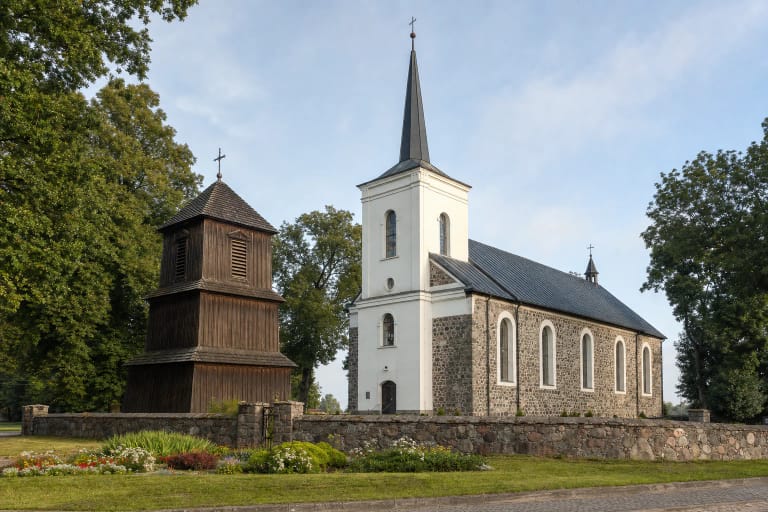 Darbėnų akmenų mūro bažnyčia su aukštu baltu bokštu, atskira trijų tarpsnių medine varpine ir lauko akmenų šventoriaus tvora