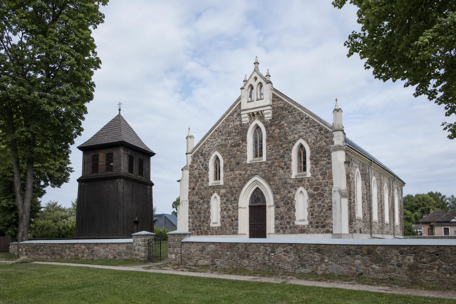 Daugų Dievo Apvaizdos bažnyčia iš lauko akmens mūro ir atskira medinė varpinė žaliame šventoriuje