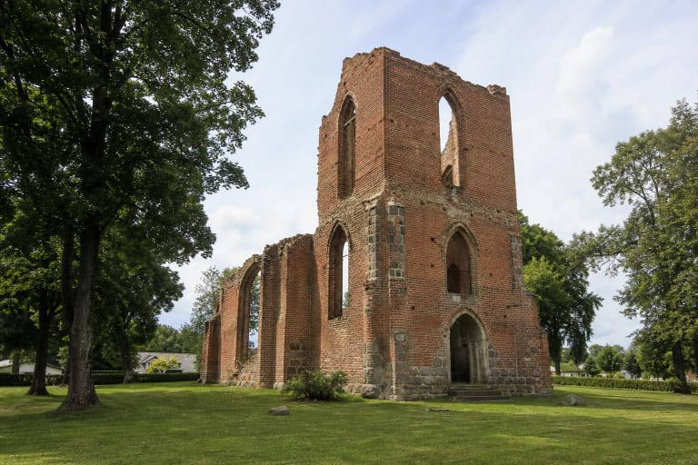 Deltuvos evangelikų reformatų bažnyčios raudonų plytų sienų ir bokšto liekanos žaliame miestelio šventoriuje