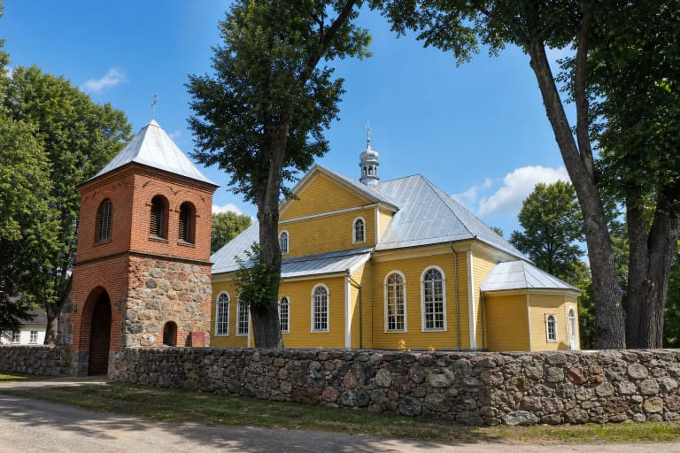 Geltona Dieveniškių medinė bažnyčia ir atskira raudonų plytų vartų varpinė už akmeninės tvoros
