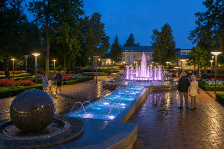 Colourfully illuminated jets of the Druskininkai Musical Fountain rising above its long basin in Spa Park at dusk