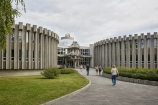 Symmetrical grey concrete wings of Druskininkai Water Park with its central glazed lobby, dome, and entrance sculpture