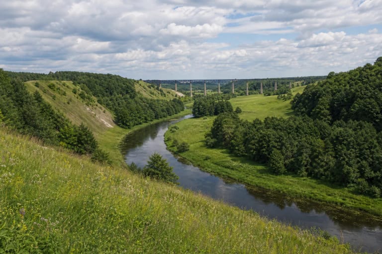 Dubysa Valley with river, green slopes, and the silhouette of Lyduvėnai railway bridge