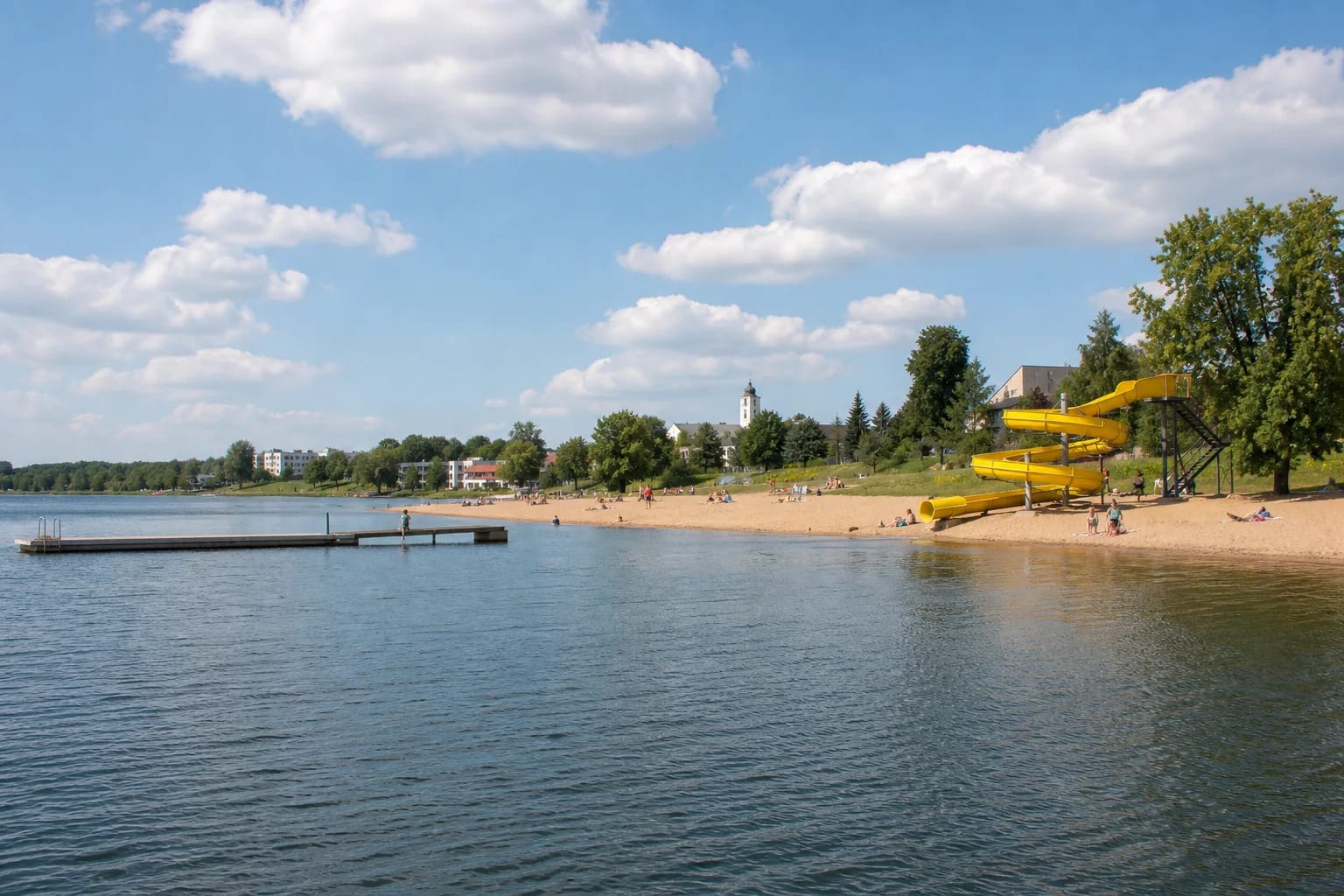 Песчаный пляж Электреная с жёлтой водной горкой, мостками и широкой гладью водохранилища в солнечный летний день