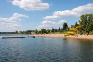Sandy Elektrėnai Beach with a yellow water slide, pier, and broad reservoir on a sunny summer day
