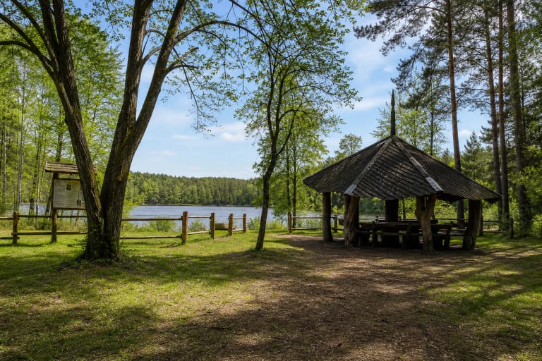 A wooden campsite pavilion, low fence, and Elniakampis Lake enclosed by wooded shores