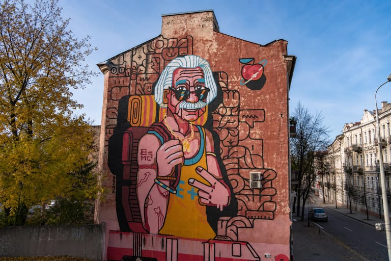 Ryški „Erasmus+“ sieninė tapyba su seno veido ir jauno kūno figūra ant Vilniaus mūro sienos