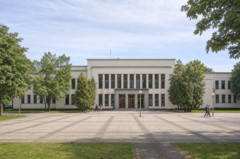 Fiziško auklėjimo rūmų Kaune šviesus simetriškas fasadas su centriniu portalu ir Ąžuolyno žaluma