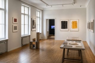 A bright compact Galerija VARTAI room with photographic works, a silkscreen piece, and a restrained sculptural installation