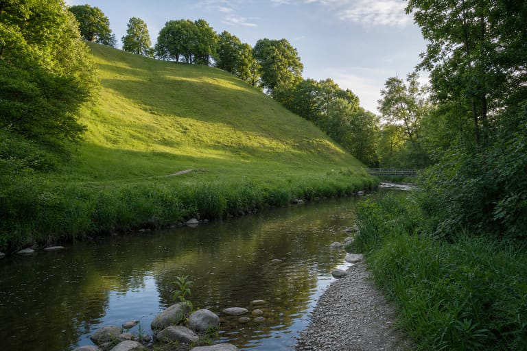 Steep green slope of Gandinga Hillfort above the winding Babrungas in a wooded valley