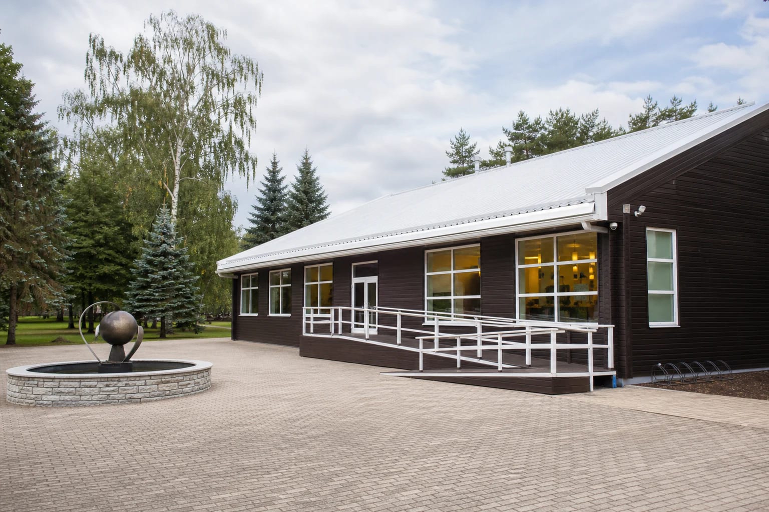 Gargždų pramogos dark timber building with a white ramp and stone fountain