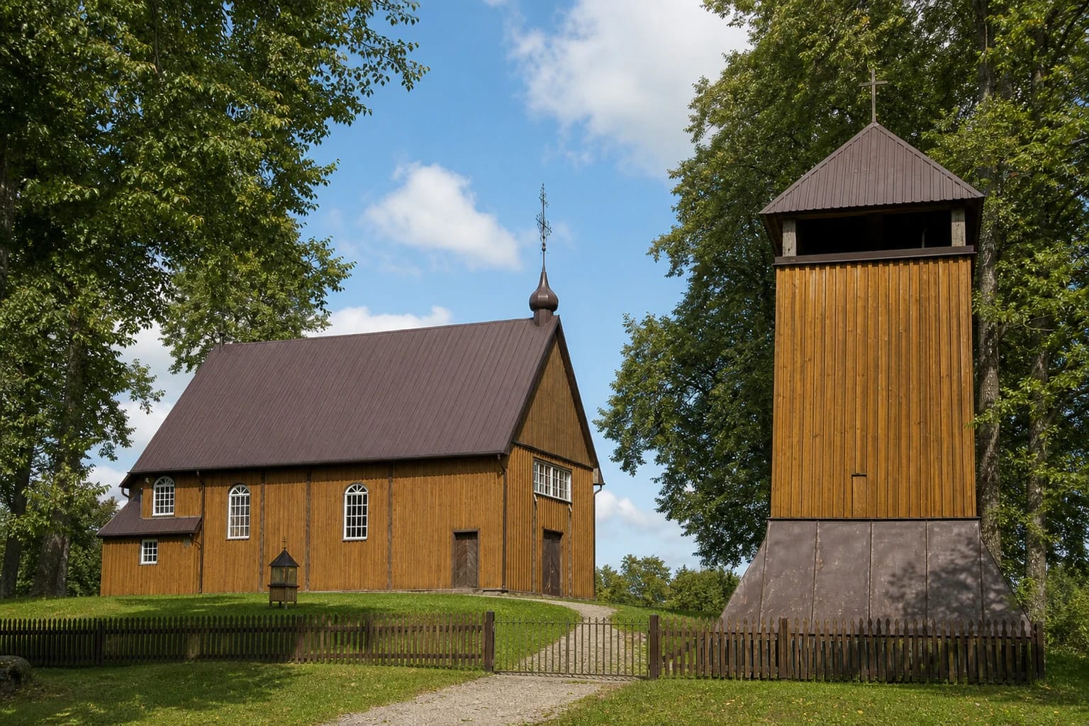 Wooden Gegrėnai Church of Jesus of Nazareth and its separate two-stage belfry in a green tree-lined churchyard
