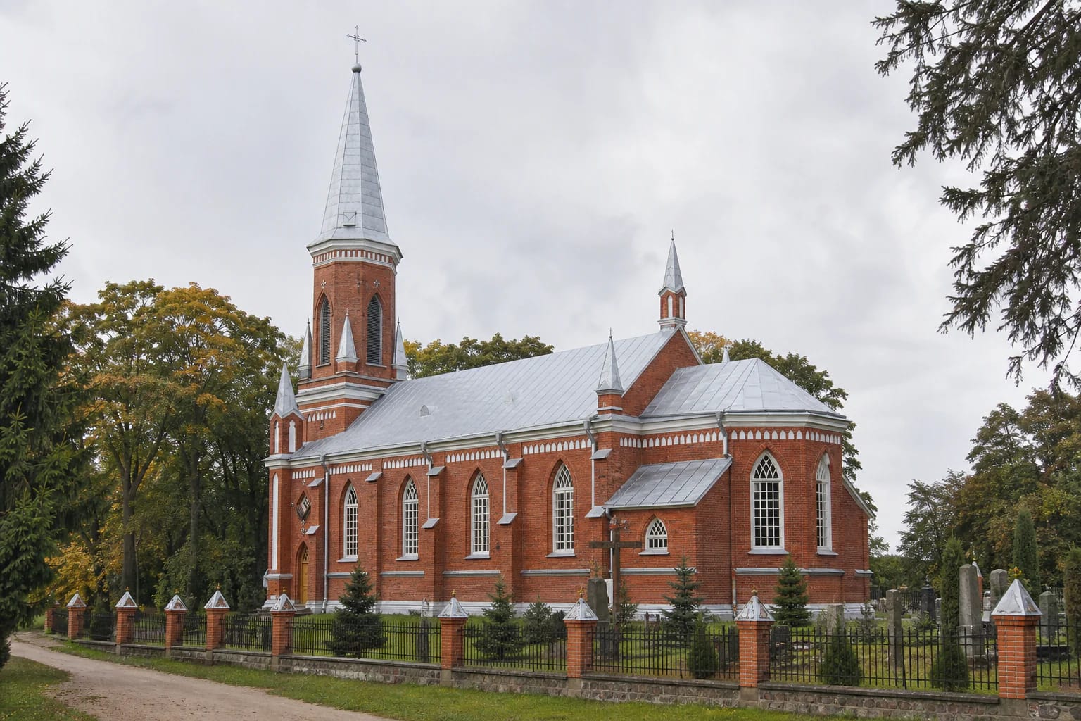 Gelgaudiškis Church of the Exaltation of the Holy Cross, a red and brown brick church with a tall tower, three turrets and a green churchyard