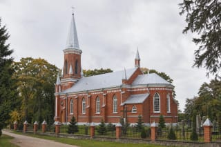 Raudonų ir rudų plytų Gelgaudiškio Šv. Kryžiaus Išaukštinimo bažnyčia su aukštu bokštu, trimis bokšteliais ir žaliu šventoriumi